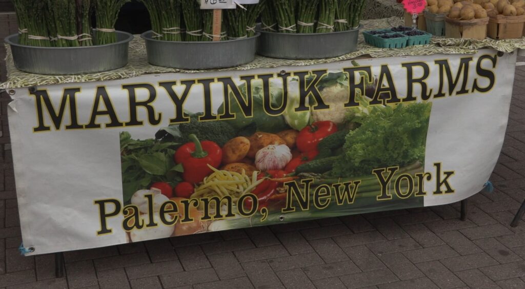 Farm stand with sign in front, displaying asparagus, blueberries and potatoes